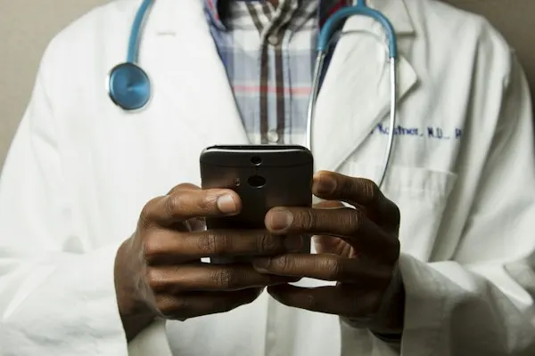Physician in a white coat and stethoscope using a smartphone